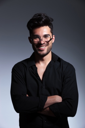 young fashion man posing with his eyeglasses upside down and smiling while holding hands crossed. isolated on a gray backgroundの写真素材