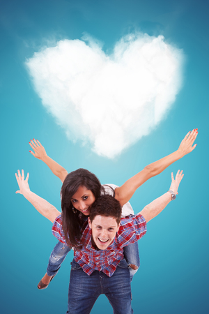 Handsome casual young man carrying his girlfriend on his back, playing in front of a heart shaped cloudの写真素材