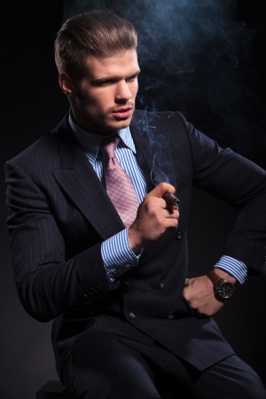 side view of a fashion business man smoking a cigar and looking away from the camera on dark backgroundの写真素材