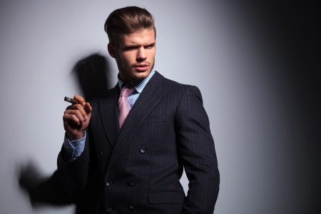 relaxed business man in a classic suit smoking a cigar and looking to his side on gray backgroundの写真素材