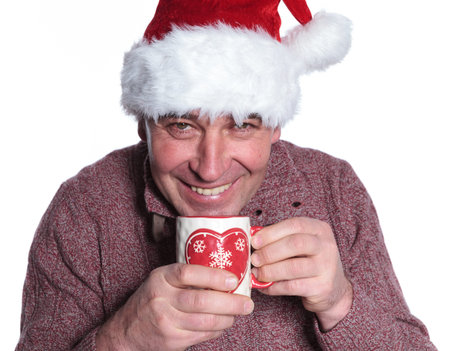 smiling old casual man wearing a santa hat  is drinking a hot tea on white backgroundの写真素材