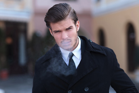 closeup portrait of an elegant young business man, outdoor, exhaling smoke while looking into the cameraの写真素材