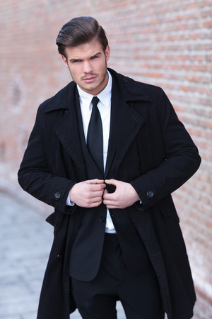 portrait of a young business man buttoning his suit outdoor while looking into the camera with a serious expressionの写真素材