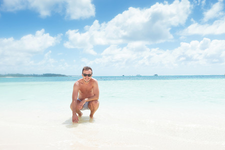 crouched man in swim suit and sunglasses on the beach of mauritiusの写真素材