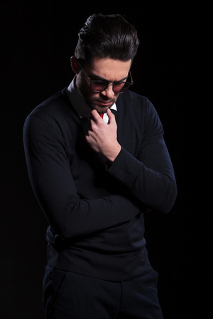 young business man looking down pensively, with his fingers on his chin. on a black backgroundの写真素材