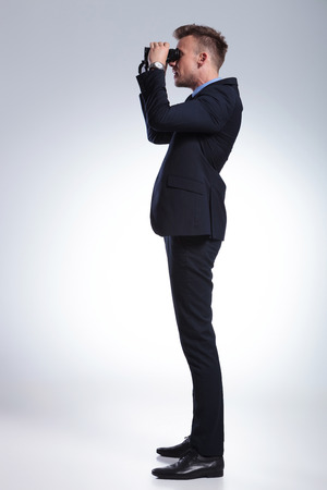 full length side view picture of a young business man looking through binoculars. on a light gray studio backgroundの写真素材