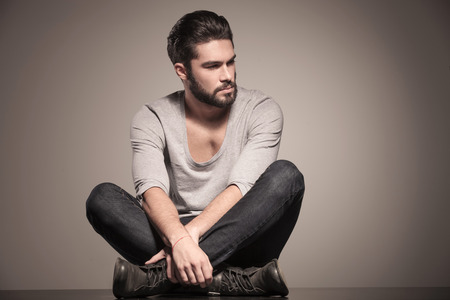 seated young man with beard is looking to his side in studioの写真素材