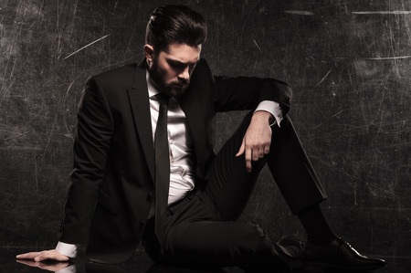 sad young bearded business man looking down while resting on the floorの写真素材