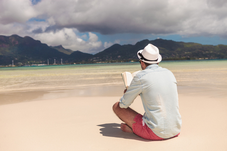 back view of a young man reading a book on the beachの写真素材