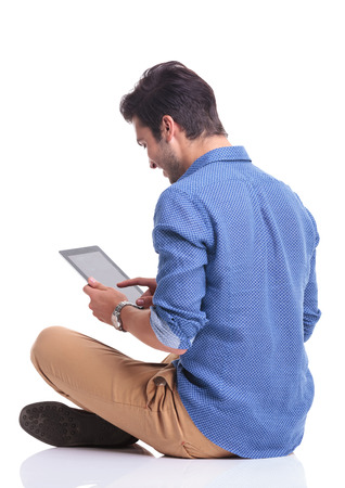 side back view of a smiling young man working on a tablet pad computer on white backgroundの写真素材
