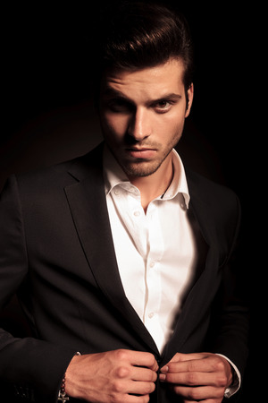 portrait of a young fashion man buttoning his suit on black studio backgroundの写真素材
