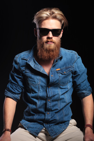 Cool fashion man wearing sunglasses and blue shirt, posing for the camera. On black background.の写真素材