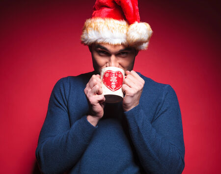 Young santa man drinking a hot tea from a white mug with a red heart.の写真素材