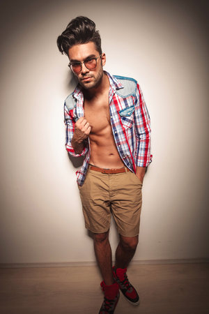 Full body image of a young fashion man pulling his shirt while looking at the camera.の写真素材