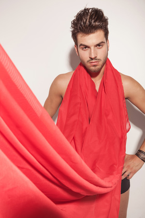 Handsome young naked man looking at the camera while holding his hand on his hip, a red scarf is covering him.の写真素材