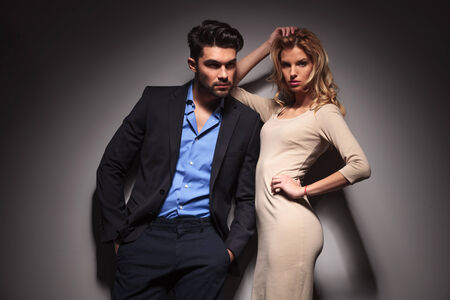 Young fashion business man looking away with his hands in pockets while his lover is leaning on him and fixing her hair.の写真素材