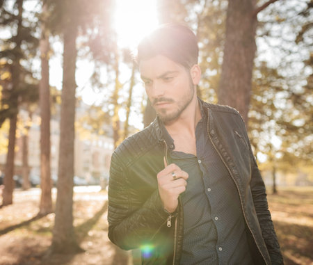 Outdoor picture of a young fashion man looking down while pulling his jacket.の写真素材