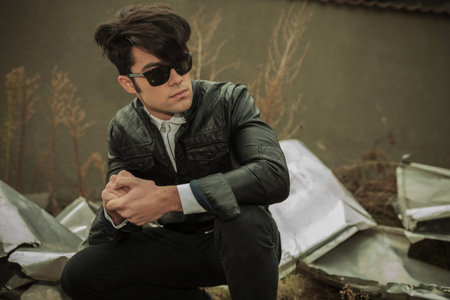 Handsome young casual man looking away while sitting and holding his hands together.
