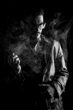 Handsome young fashion man looking away from the camera while holding a cigarette in his right hand.の写真素材