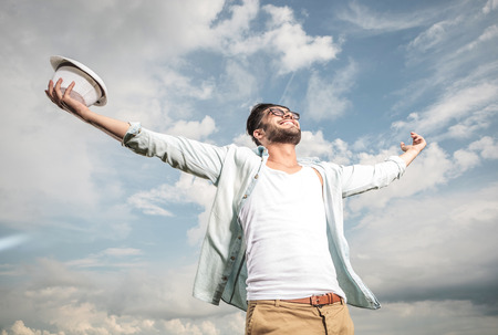 Happy young man looking up to the sky holding both hands in the air, enjoying the sun.の写真素材