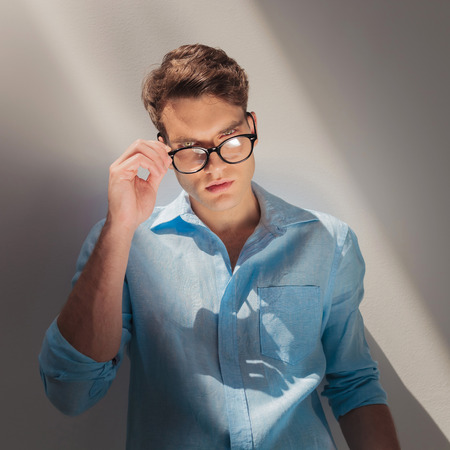 Young fashion man looking at the camera while putting on his glasses.の写真素材