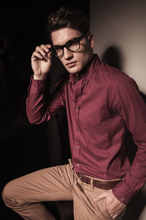 Portrait of a handsome casual business man resting his leg on a stool while fixing his glasses.の写真素材