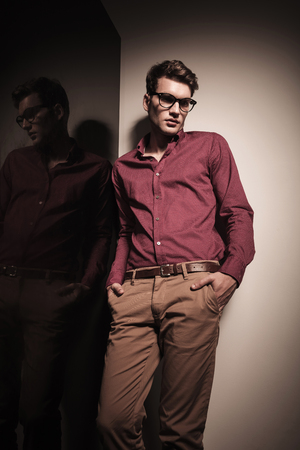 Young business man looking down while leaning on a wall with his hands in pockets.の写真素材