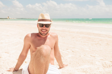 Happy man enjoying his vacation. He is sitting on the beach leaning on his hands.の写真素材
