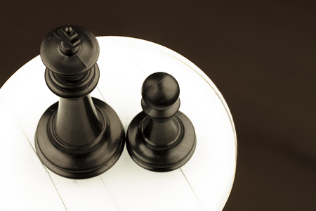 black pieces of chess, king near pawn on white circleの写真素材