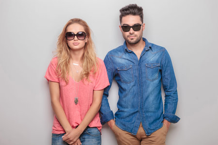 Young blonde woman holding her hands crossed while her lover is holding his hands in pockets.