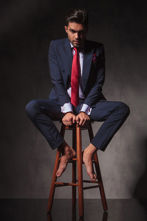 Full body of a young business man sitting on a chair while looking at the camera.の写真素材