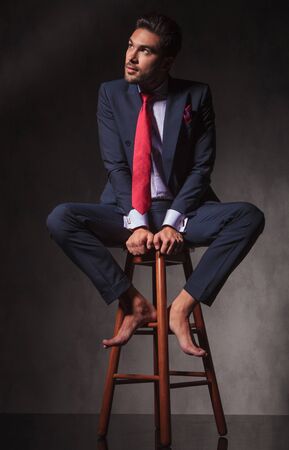 Pensive business man looking up while sitting barefoot on a stool.の写真素材