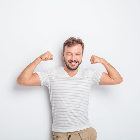 laughing young fit casual man showing you how strong he is by flexing his muscles in studio