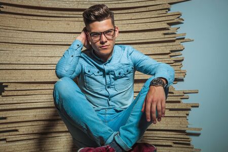 portrait of smart man wearing glasses while sitting legs crossed in wooden studioの写真素材