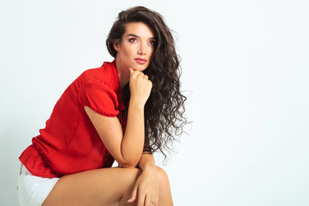 attractive woman sitting and resting her hands on her leg while looking up away off the camera