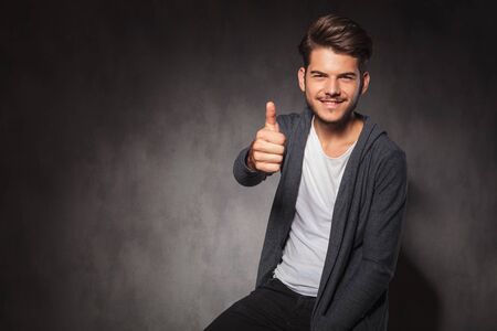 sexy man showing positive hand gesture while sitting in studio backgroundの写真素材