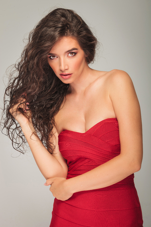 beautiful woman in sexy red dress posing while fixing her hair in studioの写真素材