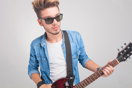 young fashion artist playing the guitar in studio background while looking awayの写真素材