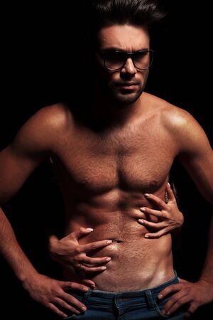 woman embracing topless muscular man from behind while he looks away with hands on waist in dark studio backgroundの写真素材