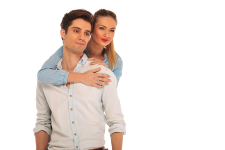 girlfriend holding man from behind while both look away from the camera in isolated studio backgroundの写真素材