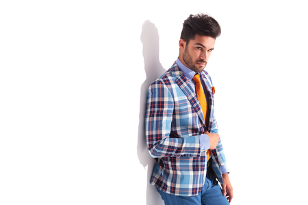 close portrait of casual man standing in studio background while fixing his plaid jacket and looking at the cameraの写真素材