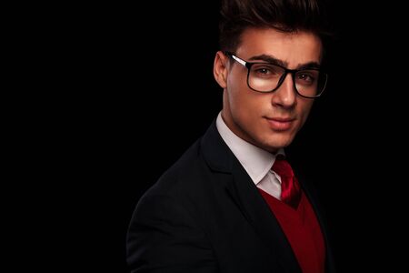 close portrait of handsome young man wearing glasses, looking at the camera while smiling in dark studio backgroundの写真素材