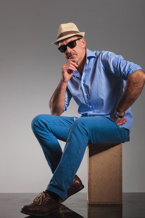 side portrait of mature man wearing hat and black sunglasses while seated and thinking.の写真素材