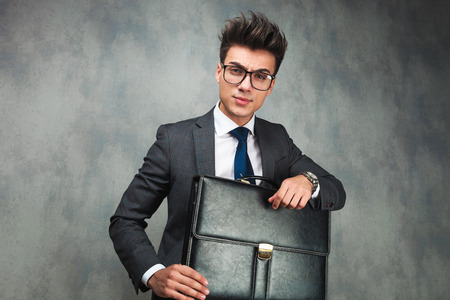 portrait of a modern business man holding a suitcase , standing against grey studio backgroundの写真素材