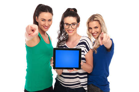 three young women presenting a tablet pad's blank screen and pointing fingers to the camera on white backgroundの写真素材