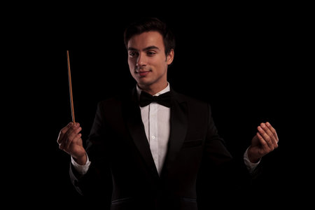 elegant man in tuxedo conducting an orchestra , business concept, on black studio background