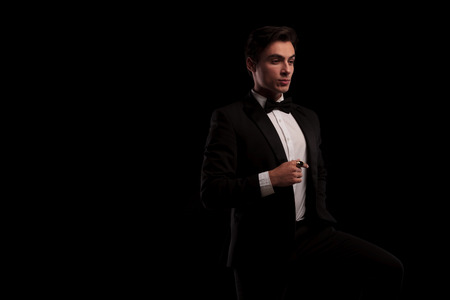 side view of an elegant man in tuxedo wearing a big gold ring and looks away from the camera on black studio background with copyspaceの写真素材