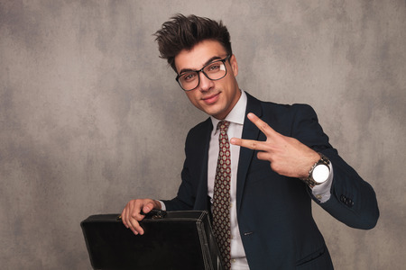 seated young business man holding briefcase and making the victory sign in studioの写真素材