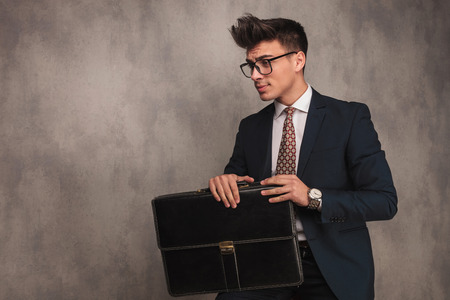 side view of a seated young business man holding briefcase and looking away to a side in studioの写真素材