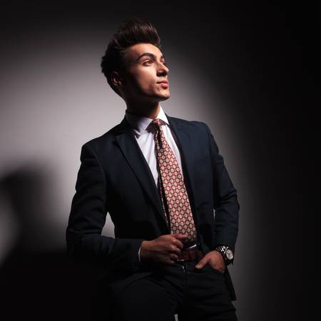 side view picture of a young business man looking up while standing with hand in pocket in studioの写真素材